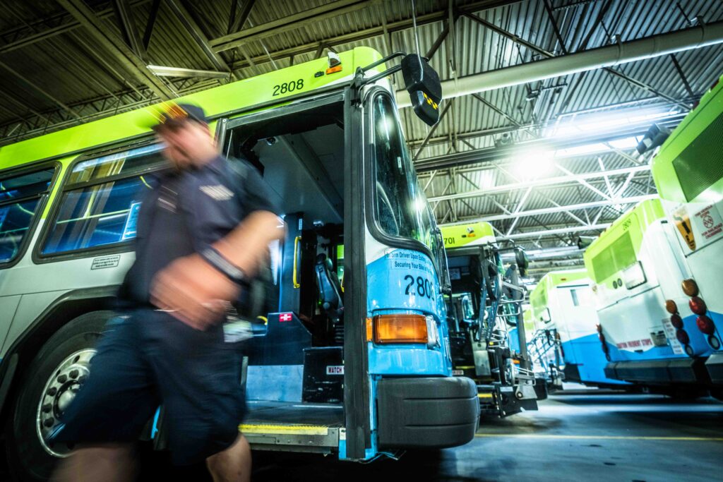 A photo of a bus driver alighting an STA bus in the STA bus garage with other STA buses in the background.