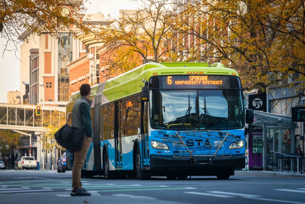 A person standing in the foreground watching an STA bus in the background in downtown Spokane