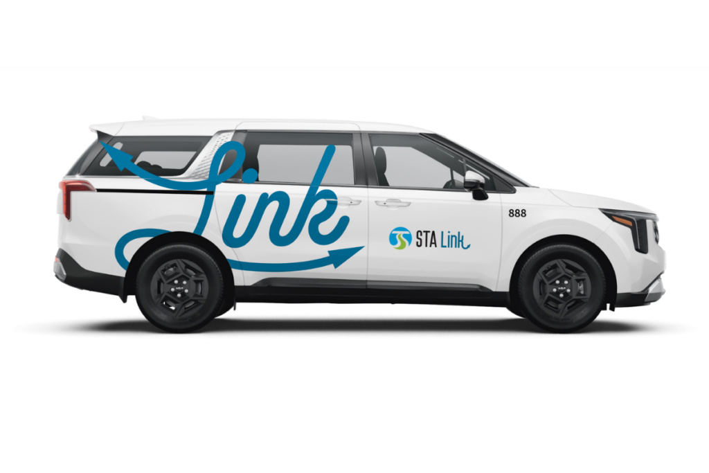 A photo of a Kia Carnival Minivan with the STA Link logo and STA logo on the side of the car.